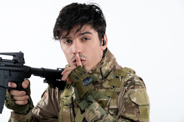 Portrait of male soldier in military uniform with machine gun white wall