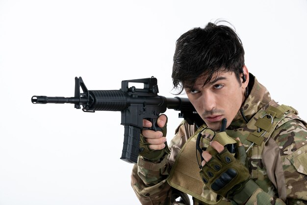 Portrait of male soldier in military uniform with machine gun white wall