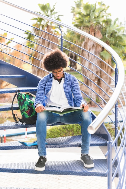 Портрет студента, сидя на синей лестнице, читая книгу на открытом воздухе