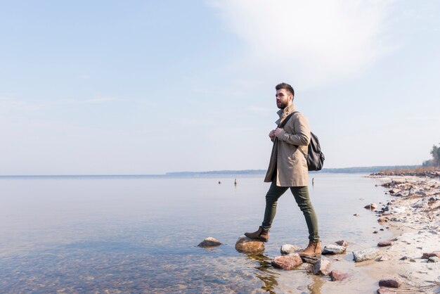 Portrait of a male traveler standing near the lake with his backpack