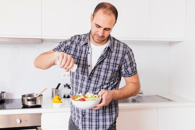 Portrait of a man adding spices in salad bowl