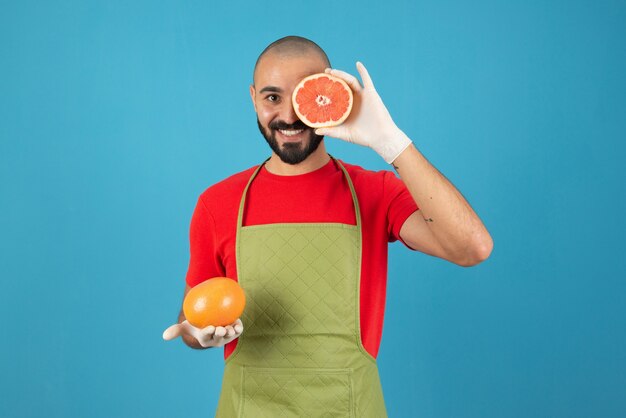 新鮮なグレープフルーツを保持しているエプロンと手袋の男の肖像画。