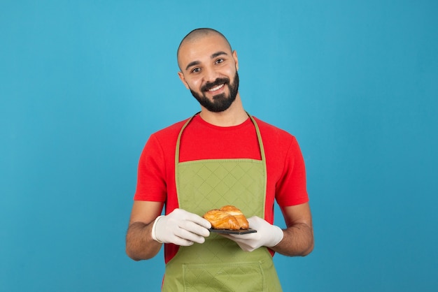 焼きたてのペストリーを保持しているエプロンと手袋の男の肖像画。