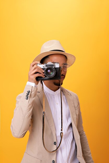 Portrait of man in beige suit taking photo on retro camera Charming guy in white tee and hat posing on isolated orange backdrop