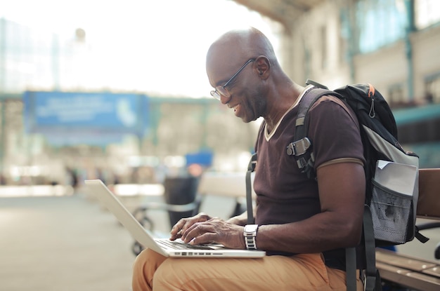portrait of man on a bench in train station while using a computer
