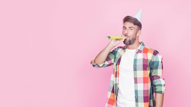 Portrait of a man blowing party horn on pink background