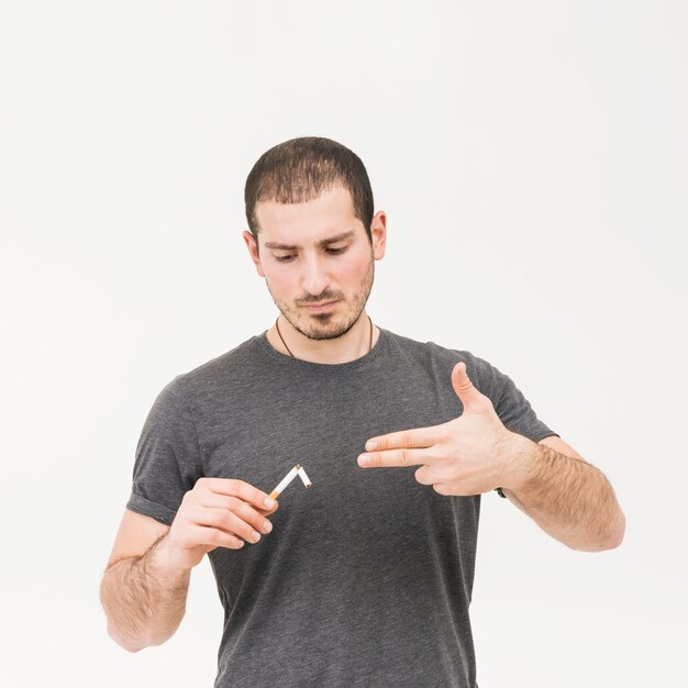 Portrait of a man holding broken cigarette making handgun gesture against white background