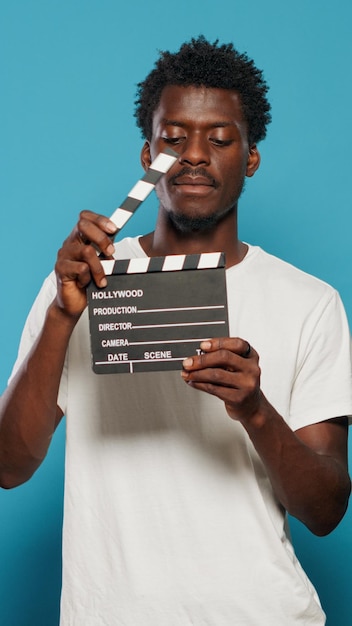 Free photo portrait of man holding clapperboard to cut scenes in movie industry. cheerful person using chalkboard for film making production and cinematography in studio. young adult with clap board