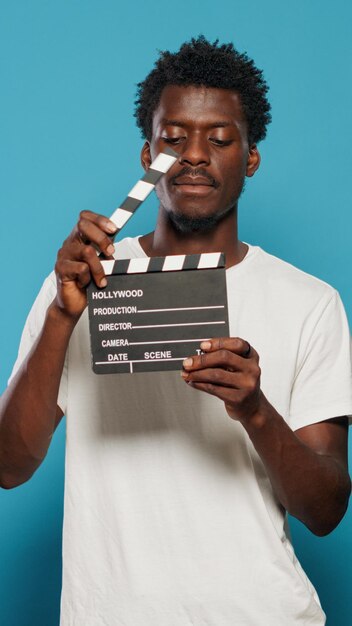 Portrait of man holding clapperboard to cut scenes in movie industry. Cheerful person using chalkboard for film making production and cinematography in studio. Young adult with clap board