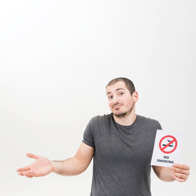 Portrait of a man holding no smoking sign shrugging against white background