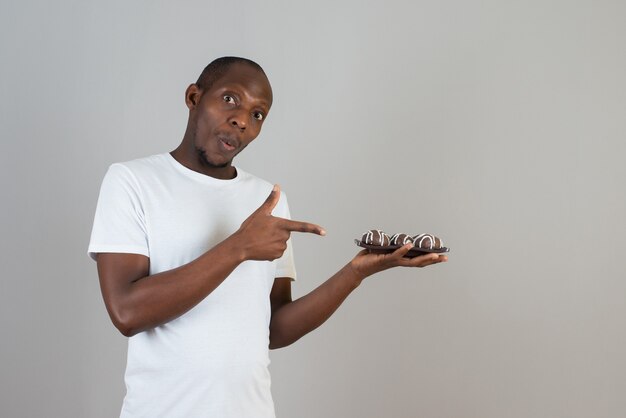 Portrait of man holding plate of sweet cookies on gray wall