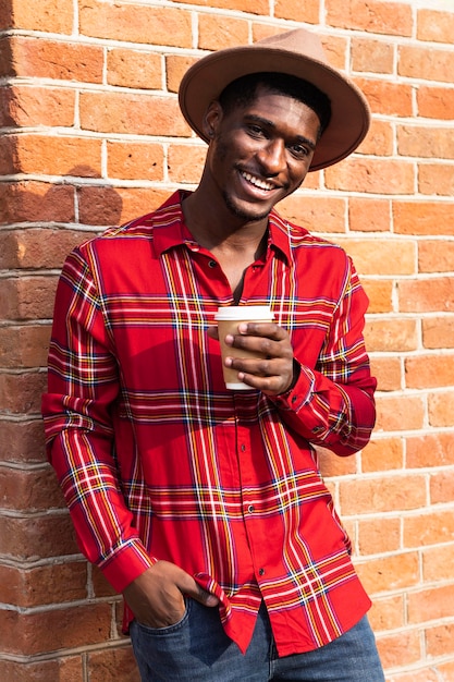 Foto gratuita ritratto di uomo appoggiato a una parete e che tiene un caffè
