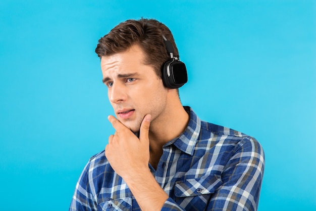 Portrait of man listening to music on wireless headphones having fun on blue