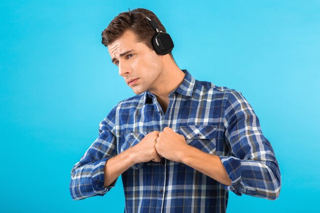 Portrait of man listening to music on wireless headphones having fun on blue