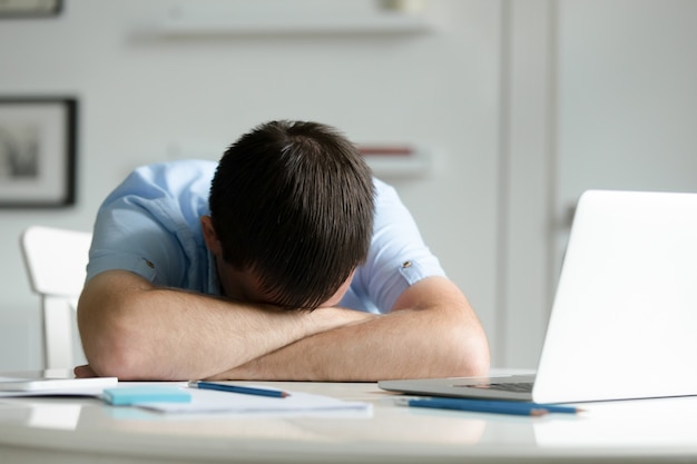 Free photo portrait of a man lying down at desk near laptop