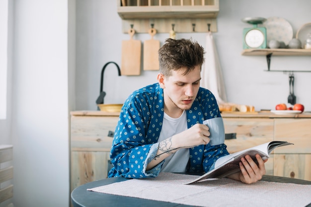 Foto gratuita ritratto del libro di lettura dell'uomo mentre bevendo caffè in cucina