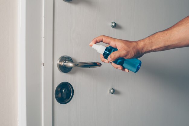 Portrait of a man at room sanitizing door handler.  