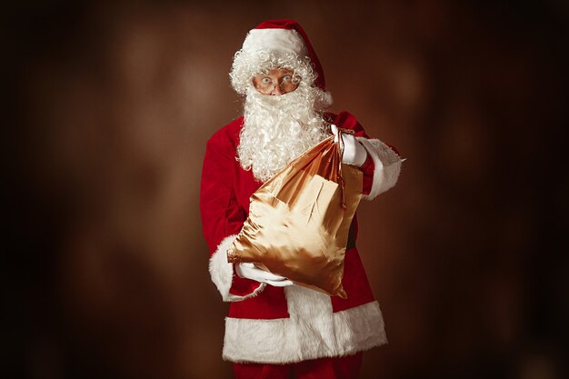산타 클로스 의상을 입은 남자의 초상화-고급스러운 흰 수염, 산타의 모자와 선물이있는 빨간 스튜디오 배경에서 빨간 의상