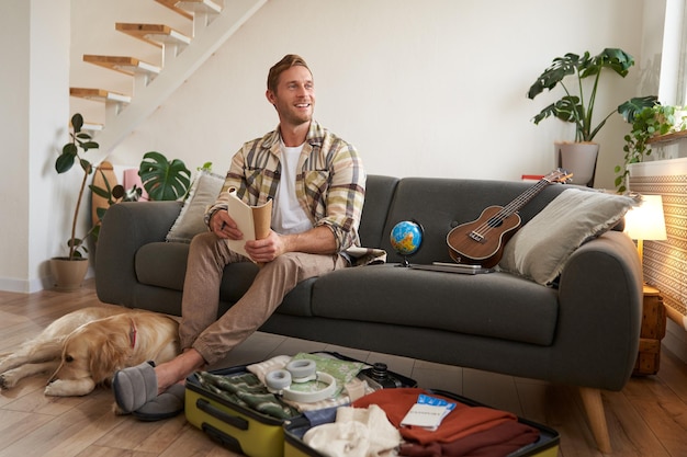 Free photo portrait of man sitting with his dog packing suitcase for a holiday going on trip with a pet