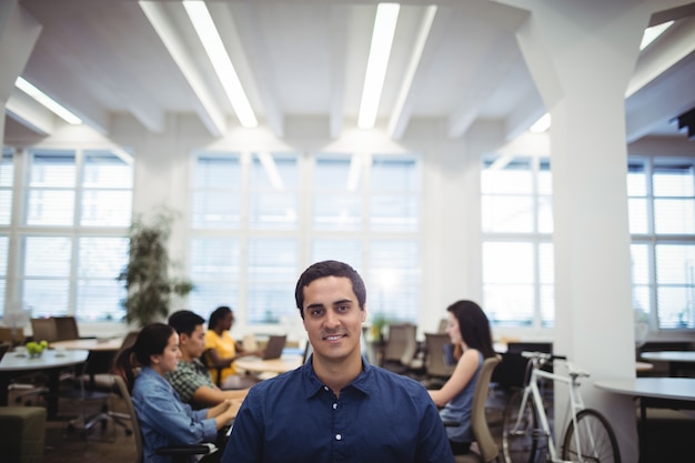 Portrait of man smiling at camera while colleagues working in ba