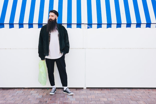 Portrait of a man standing in front of awning holding plastic carry bag