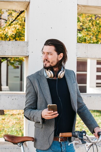 Portrait of a man standing near the wall with bicycle holding mobile phone