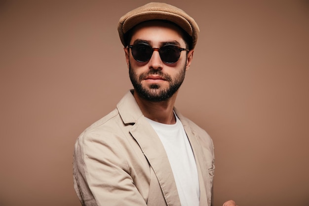 Free photo portrait of man wearing beige jacket cap and sunglasses on isolated background