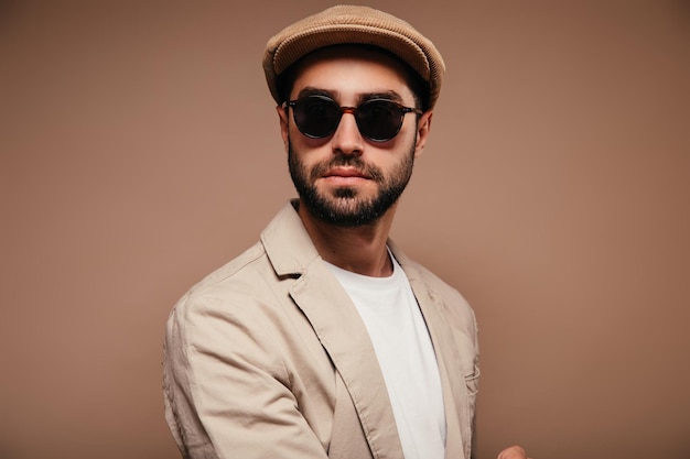 고립 된 배경에 베이지 색 재킷 모자와 선글라스를 착용 한 남자의 초상화