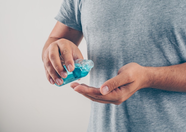 Portrait of a man at white background sanitizing his hand in gray t-shirt  