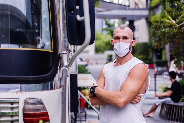 Portrait of man in white medical mask on central square in city sits on chair in van cafe