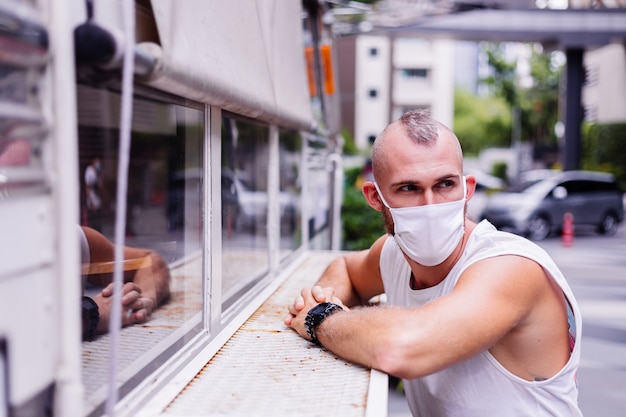 Free photo portrait of man in white medical mask on central square in city sits on chair in van cafe