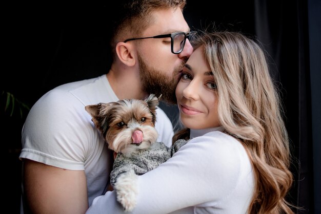 Portrait of a man who is kissing the woman's forehead and funny puppy on the hands