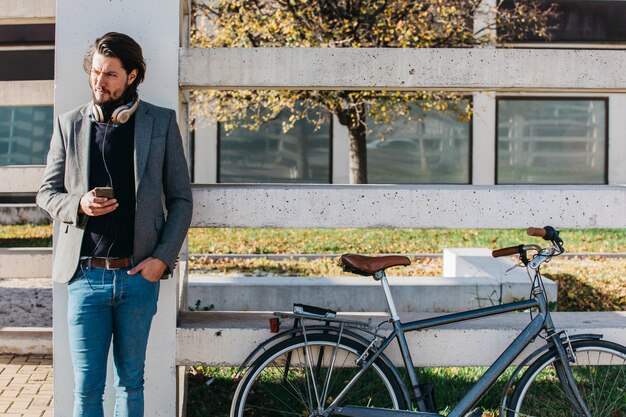 Portrait of a man with cell phone in hand standing near the bicycle