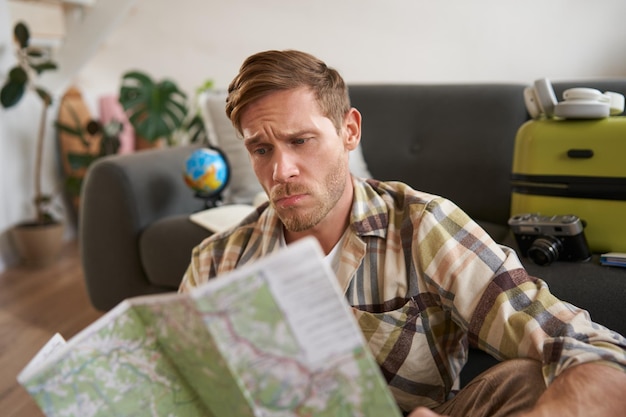 Foto gratuita ritratto di un uomo con la faccia perplessa preoccupata che guarda la mappa con le sopracciglia mentre studia il percorso seduto