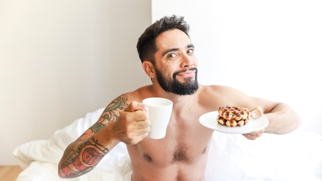 Foto gratuita ritratto di un uomo con una tazza di caffè e waffle sul piatto