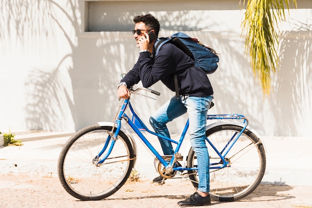 Портрет мужчины с его рюкзаком, сидя на синем велосипеде, говорить на смартфоне