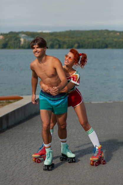 Free photo portrait of man and woman at the beach with roller skates in 80's aesthetic