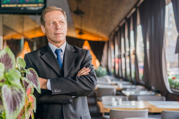 Free photo portrait of a mature businessman with crossed arms standing in restaurant