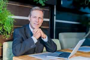 Free photo portrait of a mature businessman with laptop over desk in restaurant