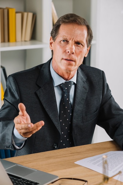 Free photo portrait of mature businessman at workplace gesturing