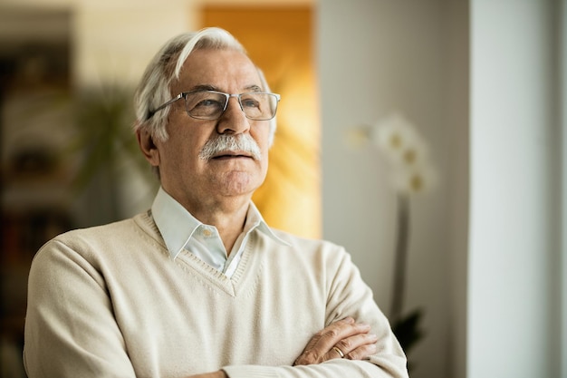 Portrait of mature man contemplating while standing with arms crossed at home