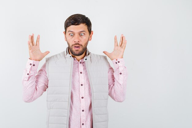 Portrait of mature man showing surrender gesture, looking down in shirt, sleeveless jacket and looking shocked front view