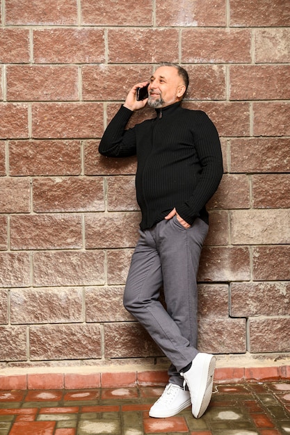 Free photo portrait of mature man standing next to brick wall