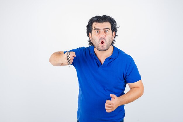 Portrait of mature man threatening with chain wrapped by fist in blue t-shirt and looking aggressive front view