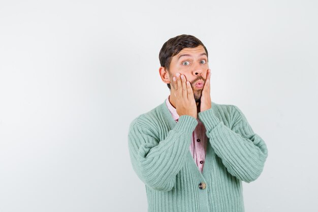 Portrait of mature man with hand on cheeks in shirt, cardigan and looking shocked front view