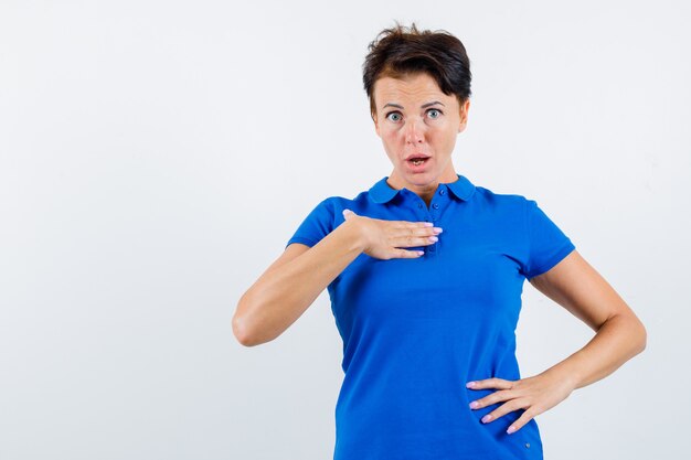 Portrait of mature woman holding hand on chest in questioning manner in blue t-shirt and looking puzzled front view