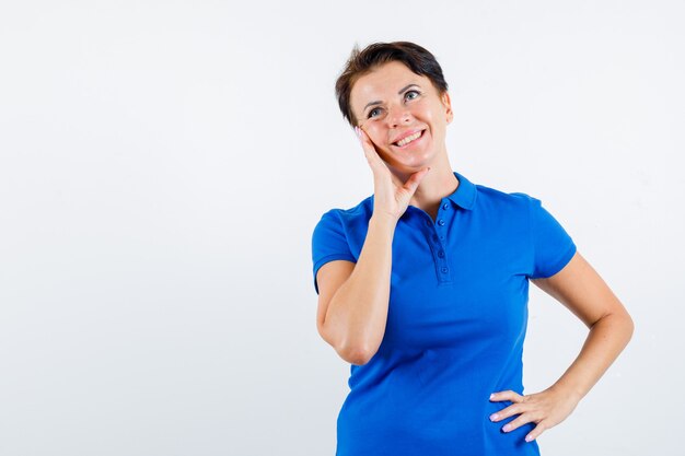 Portrait of mature woman leaning cheek on palm in blue t-shirt and looking dreamy front view