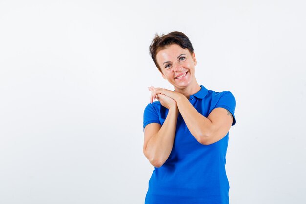 Портрет зрелой женщины, позирующей со сложенными руками в синей футболке и веселой смотрящей спереди