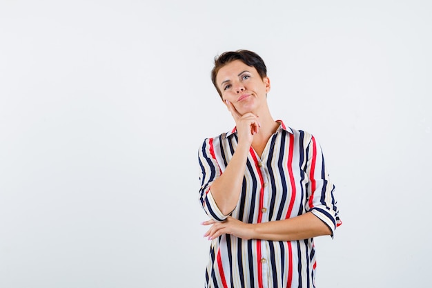 Портрет зрелой женщины, подпирающей подбородок рукой в полосатой рубашке и задумчивой смотрящей спереди