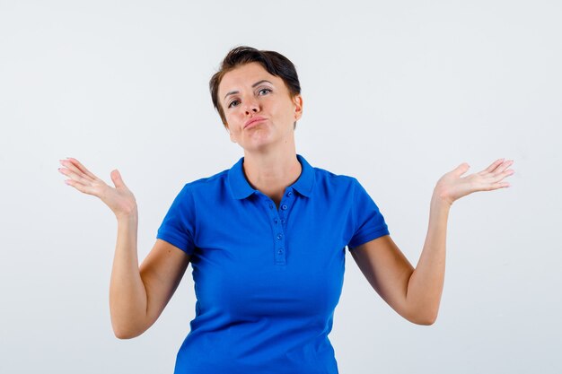 Portrait of mature woman showing helpless gesture in blue t-shirt and looking hesitant front view